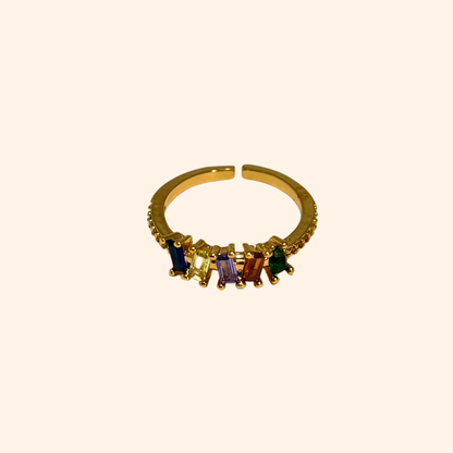 The Five Gems Gold Ring by Roots Jewellery features a dazzling arrangement of five rectangular zircons in vibrant hues—red, green, purple, blue, and clear—set diagonally.