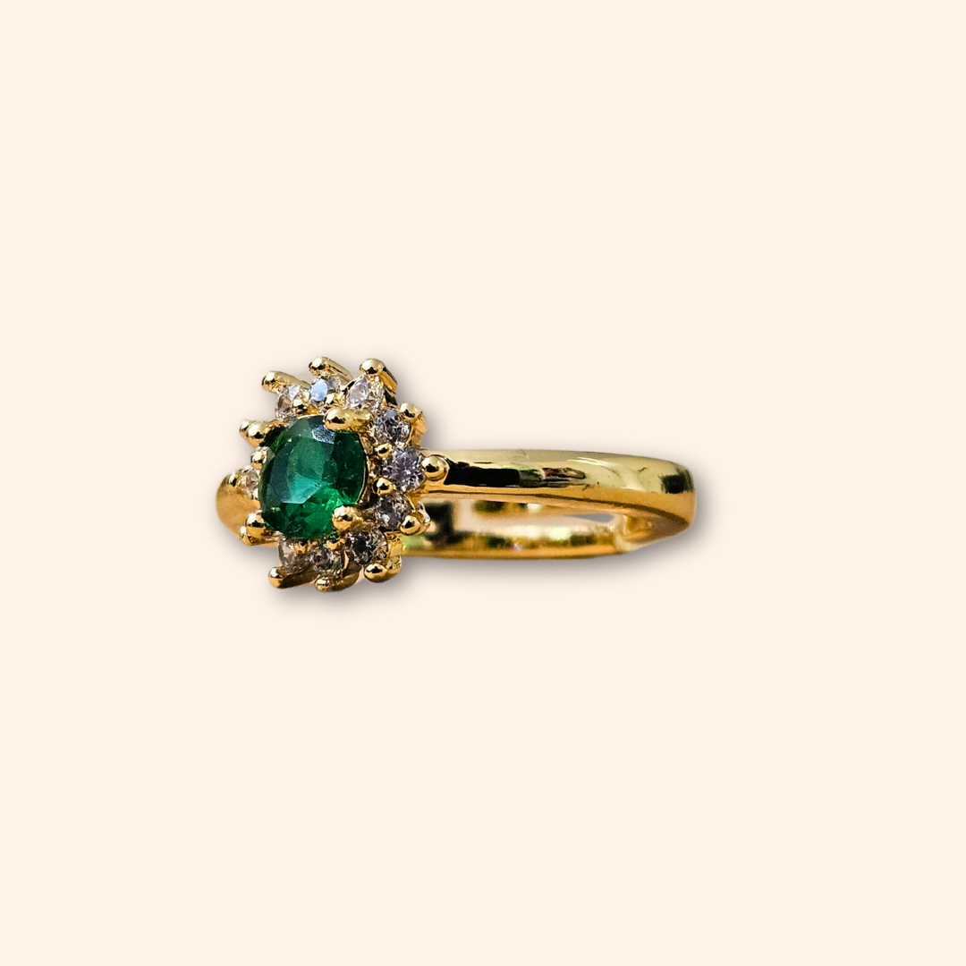 The Emerald Flower Gold Ring by Roots Jewellery features a stunning green emerald at its center, accented by dazzling clear stones. Its sophisticated design is set on a simple backdrop and includes an adjustable feature for the ideal fit.