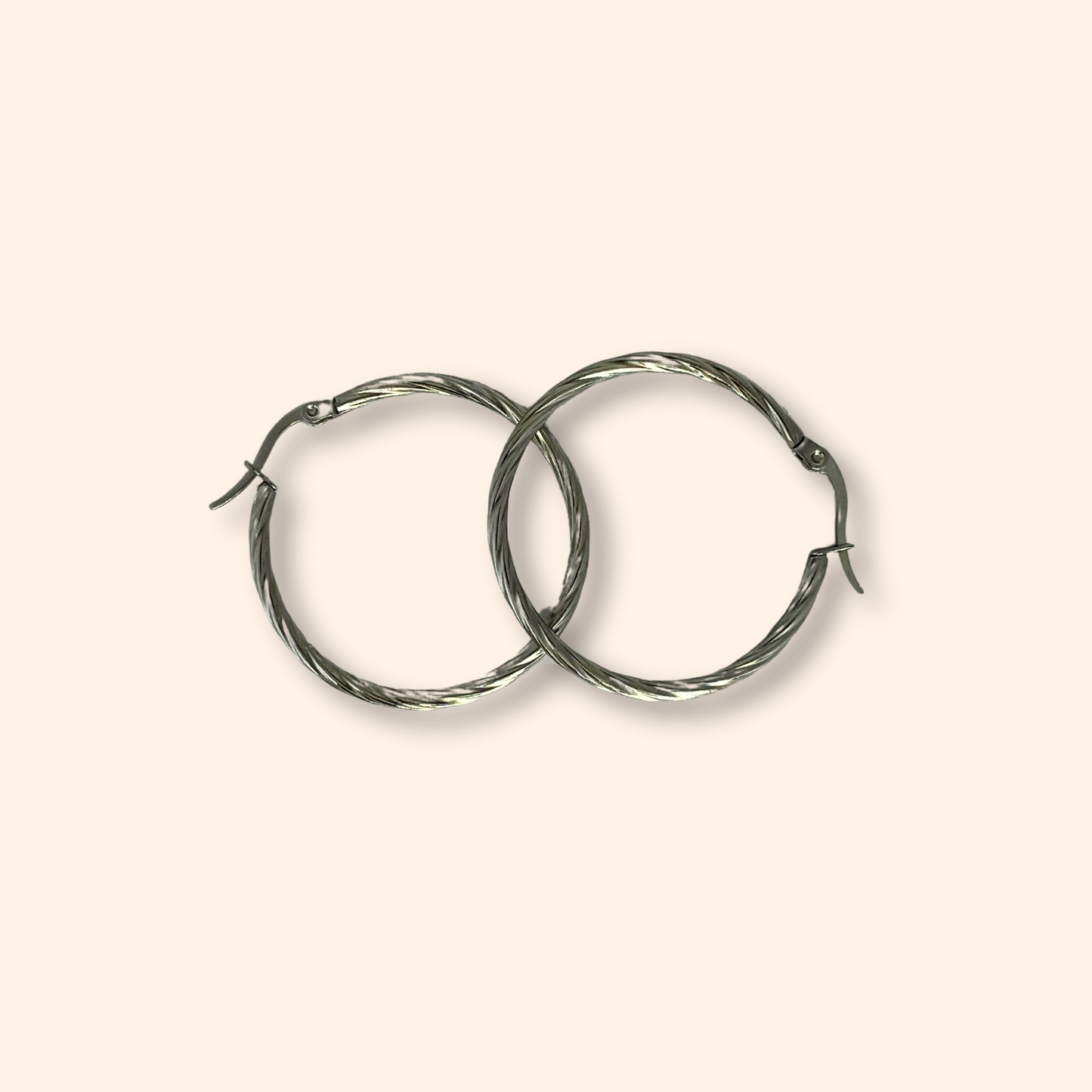 Two Roots Jewellery Silver Medium Spiral Hoop Earrings, made from stainless steel featuring a twisted design, are elegantly showcased on a neutral background.