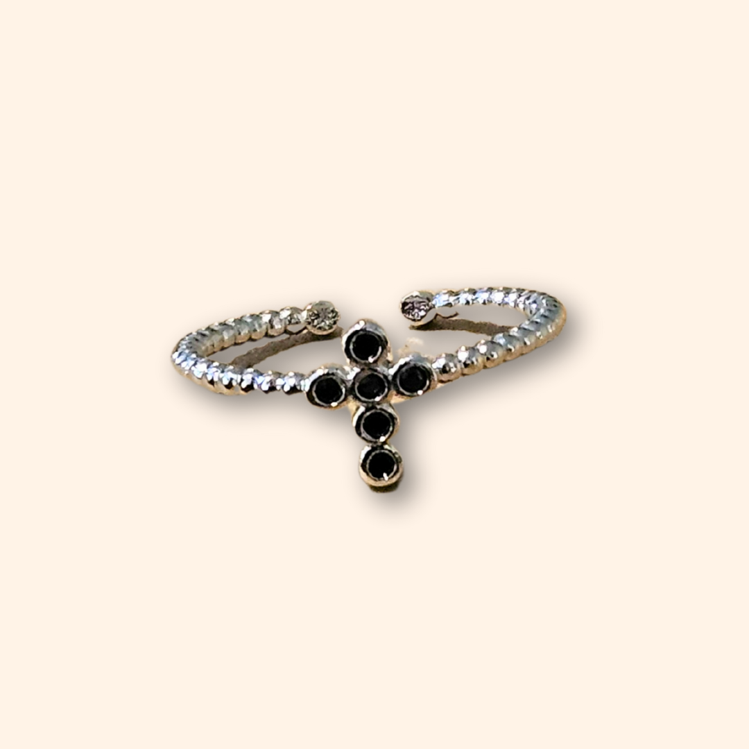 The Cross Silver Ring from Roots Jewellery is rhodium plated and showcases a striking cross design adorned with small black stones against a pale background. This adjustable ring guarantees a perfect fit for any wearer.