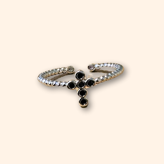 The Cross Silver Ring from Roots Jewellery is rhodium plated and showcases a striking cross design adorned with small black stones against a pale background. This adjustable ring guarantees a perfect fit for any wearer.