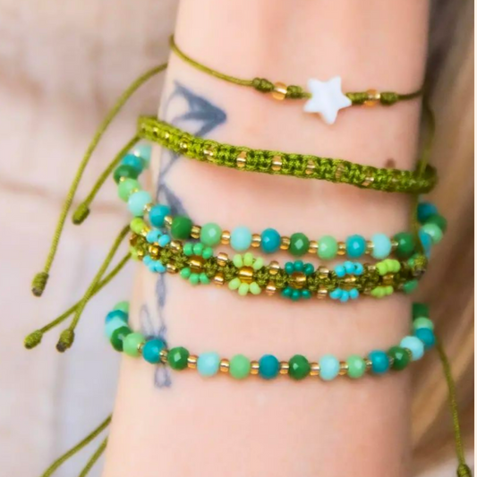 A forearm adorned with Roots Jewellery's Verdant Harmony 5-Set Bracelet, featuring handmade green and turquoise beads that highlight artisanal craftsmanship and a charming star pendant, with a hint of Bohemian style tattooed below.