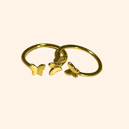 Embrace sophistication with the Butterfly Gold Ring from Roots Jewellery. This adjustable ring showcases two butterfly-shaped accents in black and green enamel against a beige background, providing both style and comfort. It's an exquisite addition to any jewelry collection.