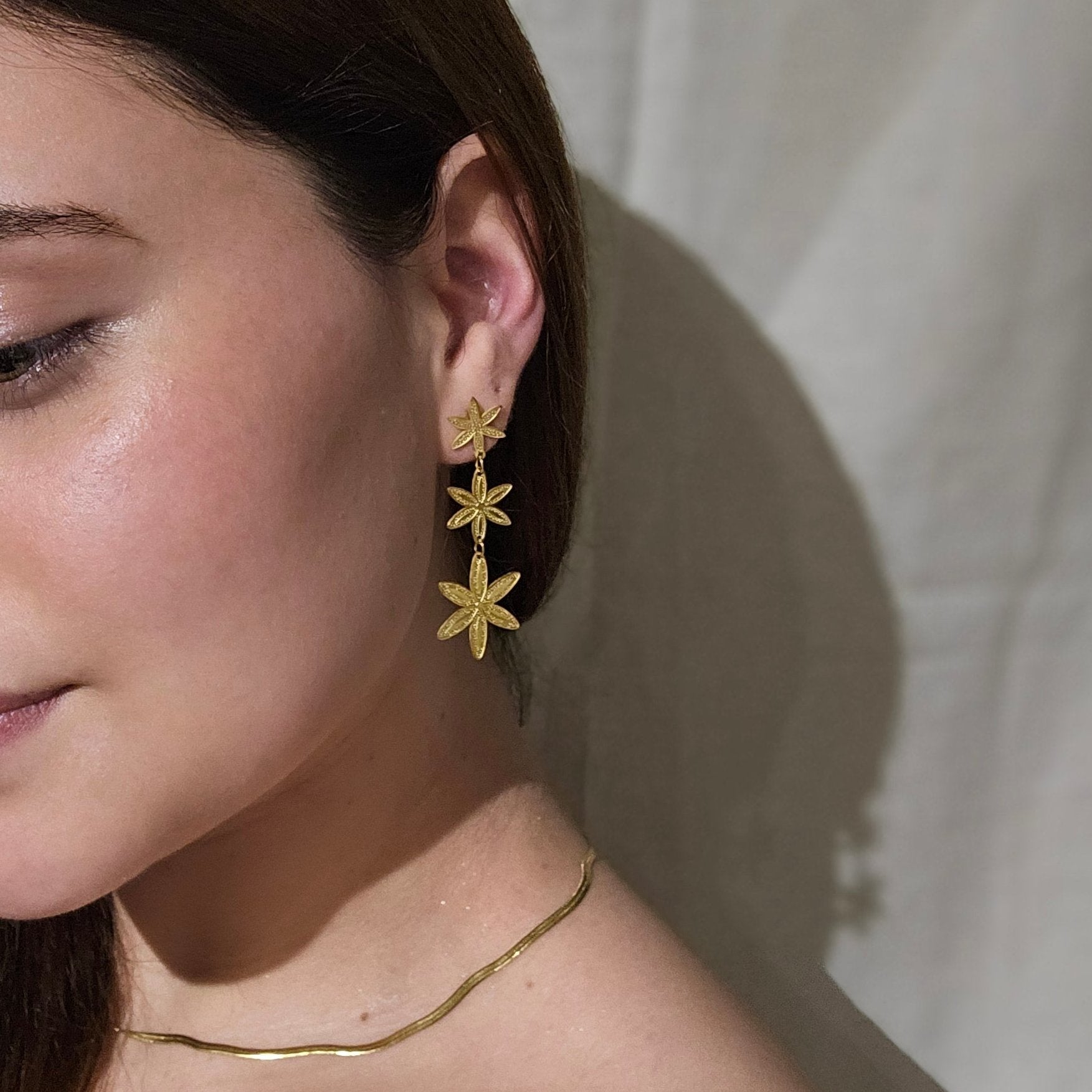 Close-up of a person elegantly adorned in golden flowers, featuring the Golden Flower Rain Earrings by Roots Jewellery and a matching gold necklace.