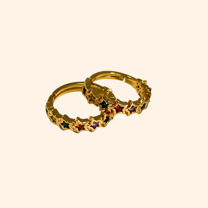 The Rainbow Stars Gold Ring from Roots Jewellery captivates with its star pattern, each embellished with shimmering gemstones. Its simple background is elevated by rhodium plating, providing a sleek finish. The adjustable design guarantees a perfect fit for any occasion.