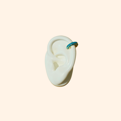 The Single Colour C Shape - Ear Cuff by Roots Jewellery is a small gold and teal ear cuff that elegantly showcases its intricate gold design, set against a beige background, highlighting this exquisite jewelry accessory.