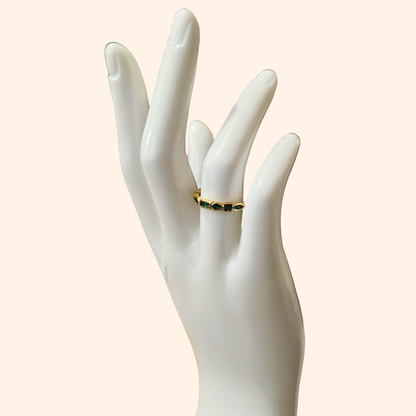 Eternity Green Gold Ring by Roots Jewellery featuring vibrant emerald zircons set in a continuous pattern on a plain beige background.