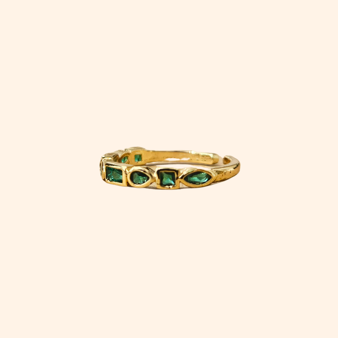 Eternity Green Gold Ring by Roots Jewellery featuring vibrant emerald zircons set in a continuous pattern on a plain beige background.