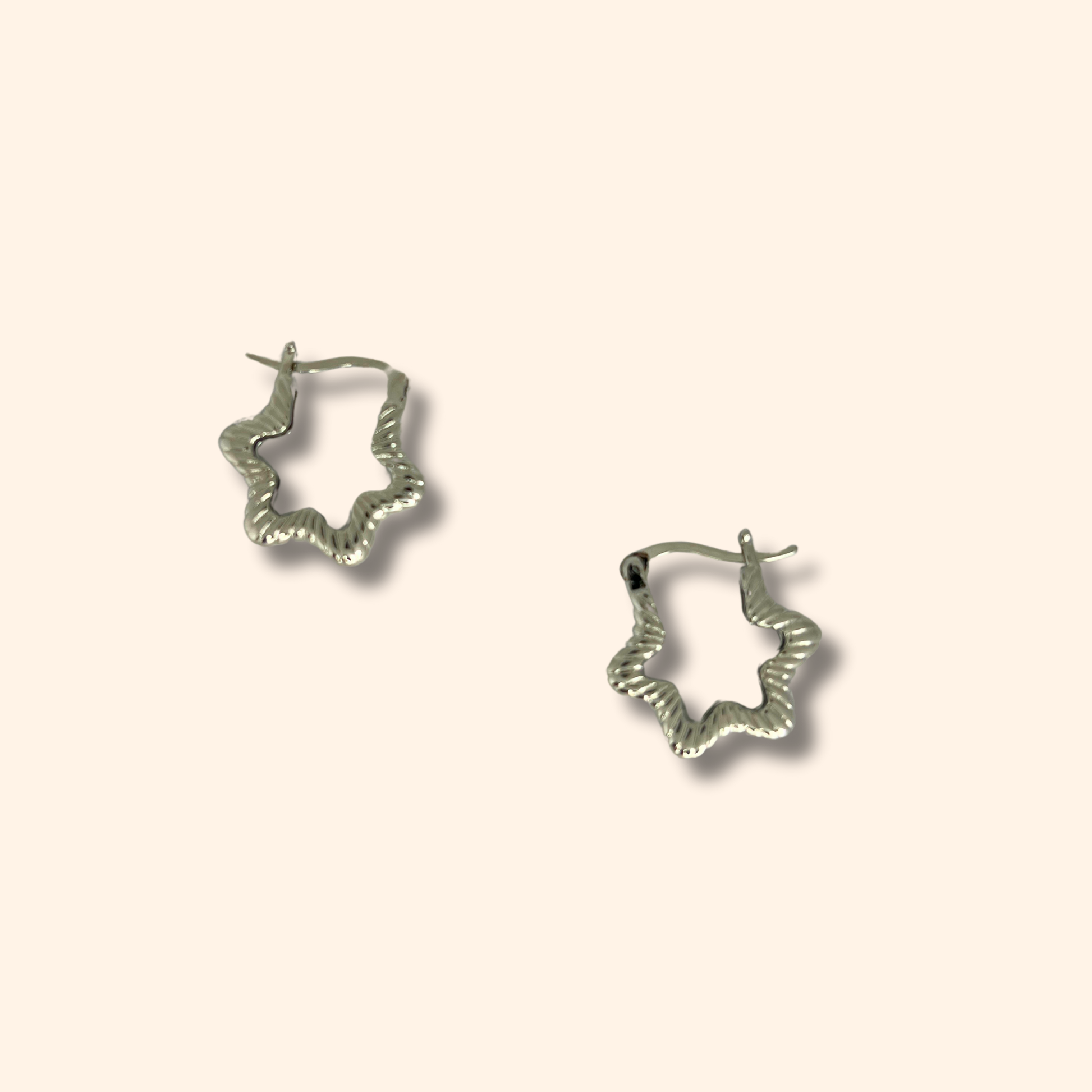 Experience the elegance of Roots Jewellery's Silver Star Hoop Earrings, rhodium-plated and showcasing a captivating star design that stands out beautifully against a simple beige backdrop.