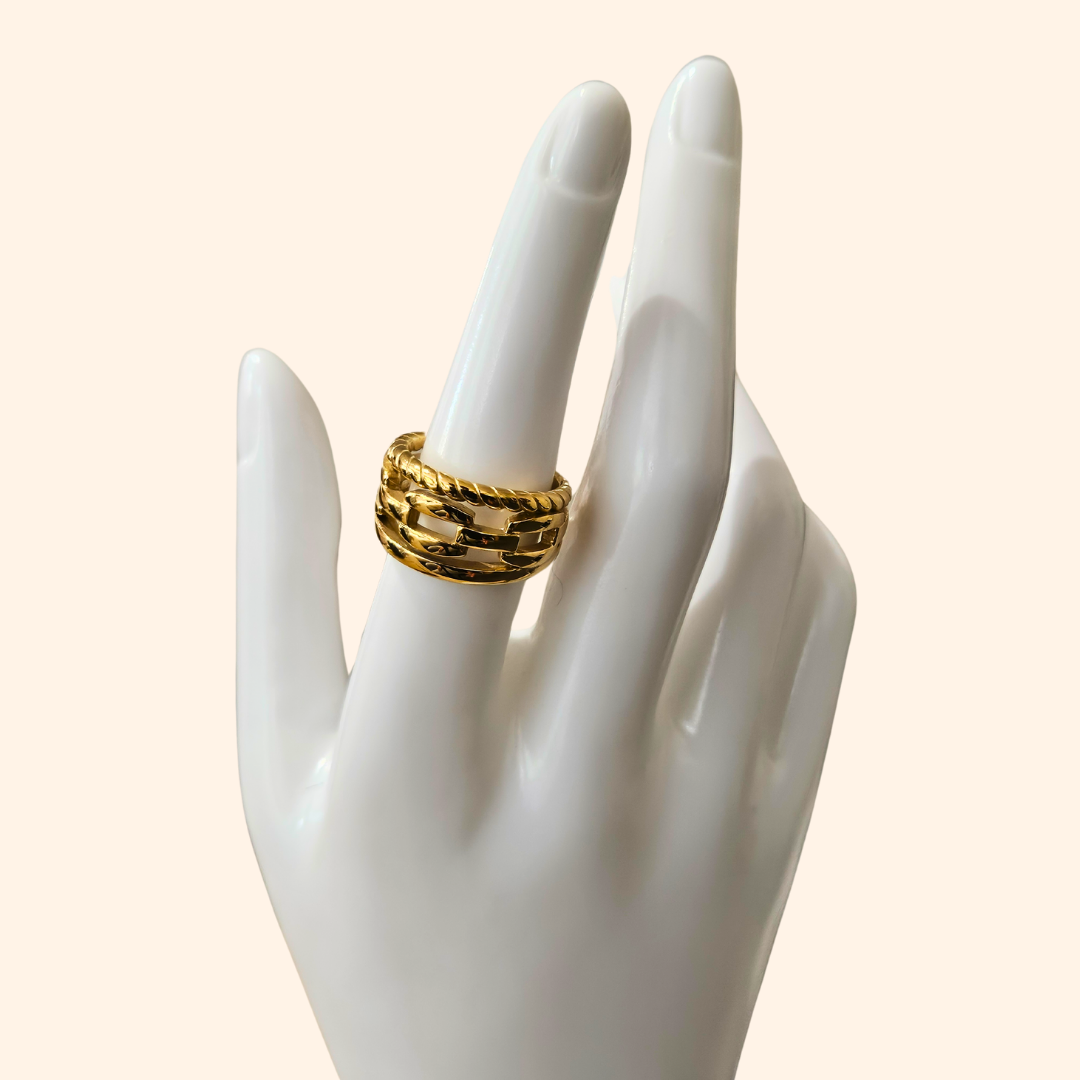 A Chain Gold Ring by Roots Jewellery, featuring a timeless interwoven design, graces a beige background.