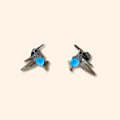 Two Silver and Blue Bird Earrings by Roots Jewellery, featuring stainless steel wings and a blue body, rest elegantly on a neutral background—perfect for animal lovers.