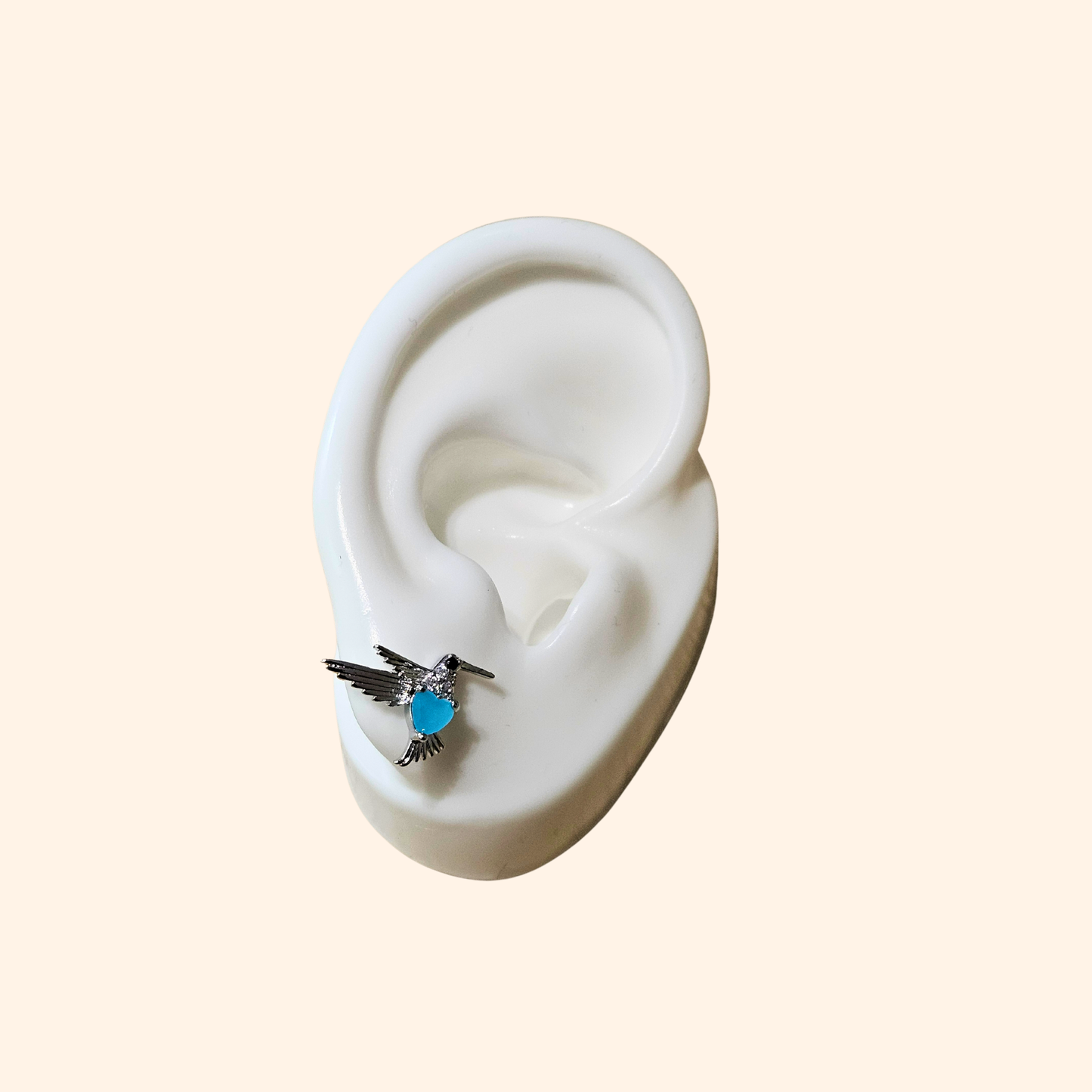 Two Silver and Blue Bird Earrings by Roots Jewellery, featuring stainless steel wings and a blue body, rest elegantly on a neutral background—perfect for animal lovers.