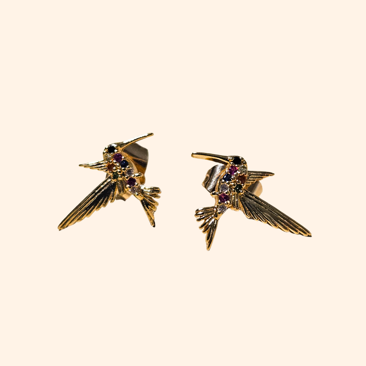 A pair of Rainbow Gold Hummingbird Earrings by Roots Jewellery, adorned with purple gem accents on a white backdrop and crafted with vibrant multicolour zircons for an extra touch of sparkle.