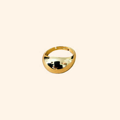 A polished Dome Gold Ring from Roots Jewellery, featuring a smooth and reflective surface, is set against a plain beige background, highlighting its elegant appeal as a jewelry accessory.