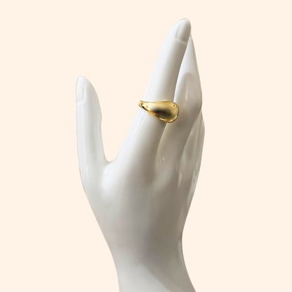 A polished Dome Gold Ring from Roots Jewellery, featuring a smooth and reflective surface, is set against a plain beige background, highlighting its elegant appeal as a jewelry accessory.