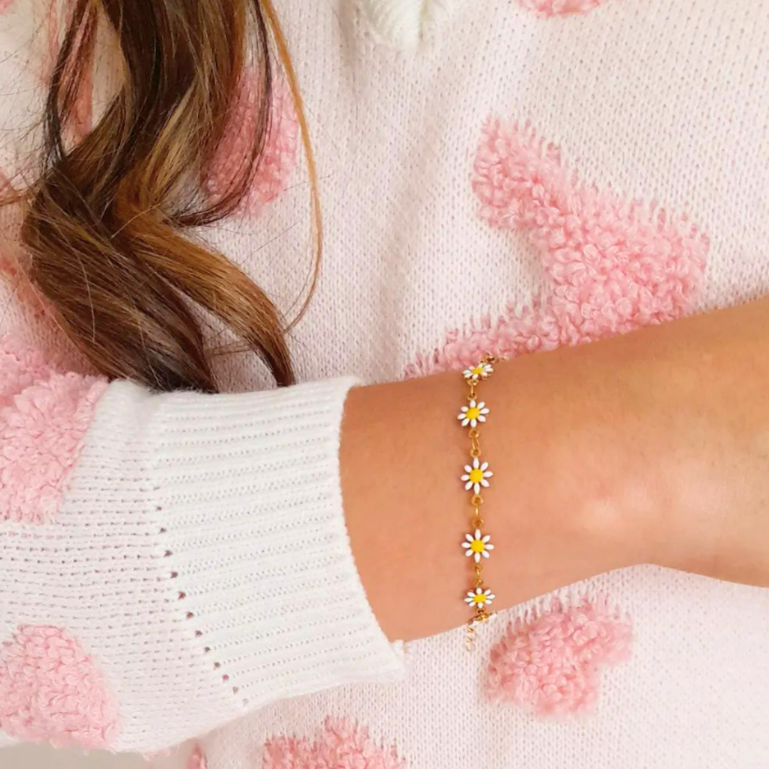 An individual is wearing a pink and white sweater, complemented by their wrist adorned with the Daisy Flower Bracelet from Roots Jewellery, a piece inspired by nature and featuring delicate gold daisy flowers.