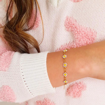 An individual is wearing a pink and white sweater, complemented by their wrist adorned with the Daisy Flower Bracelet from Roots Jewellery, a piece inspired by nature and featuring delicate gold daisy flowers.