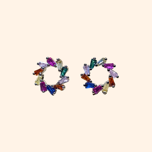 A pair of stud earrings from Roots Jewellery, featuring multicolour cubic zirconia stones artistically arranged in a spiral on a beige background.