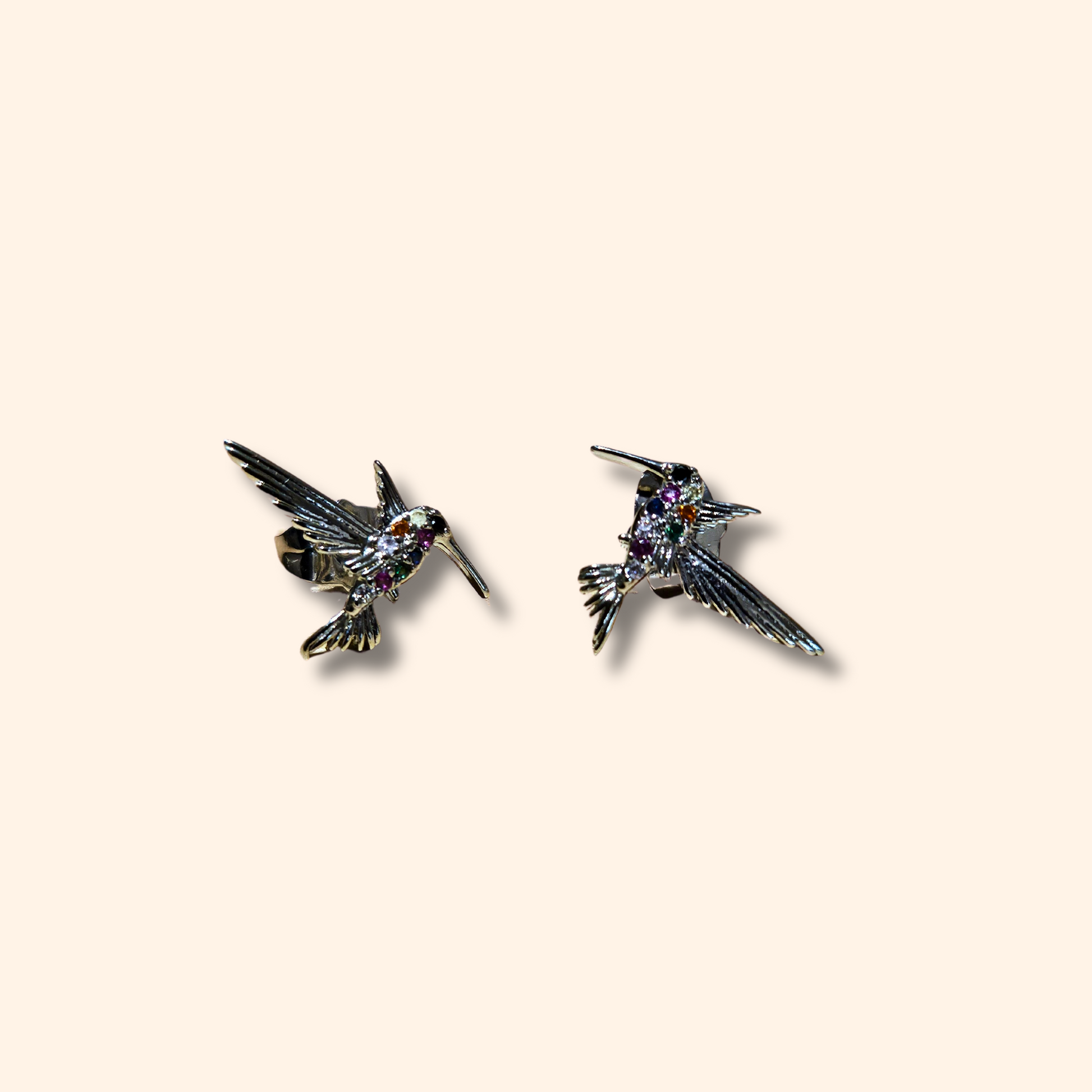 Two sparkling, silver-colored hummingbird earrings with detailed designs on a plain background from Roots Jewellery's Rainbow Silver collection.