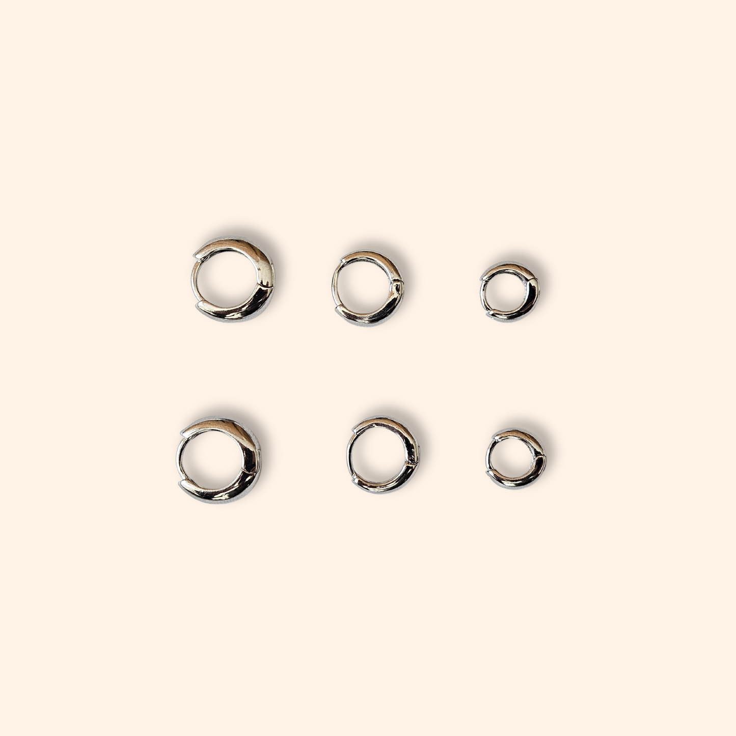 Five pairs of exquisite hoop earrings from the Roots Jewellery's "3 Set Hoop Earrings" collection gleam on a light beige background, showcasing their stunning elegance. Available in both gold and silver finishes, these elegant pieces are perfect for any occasion.