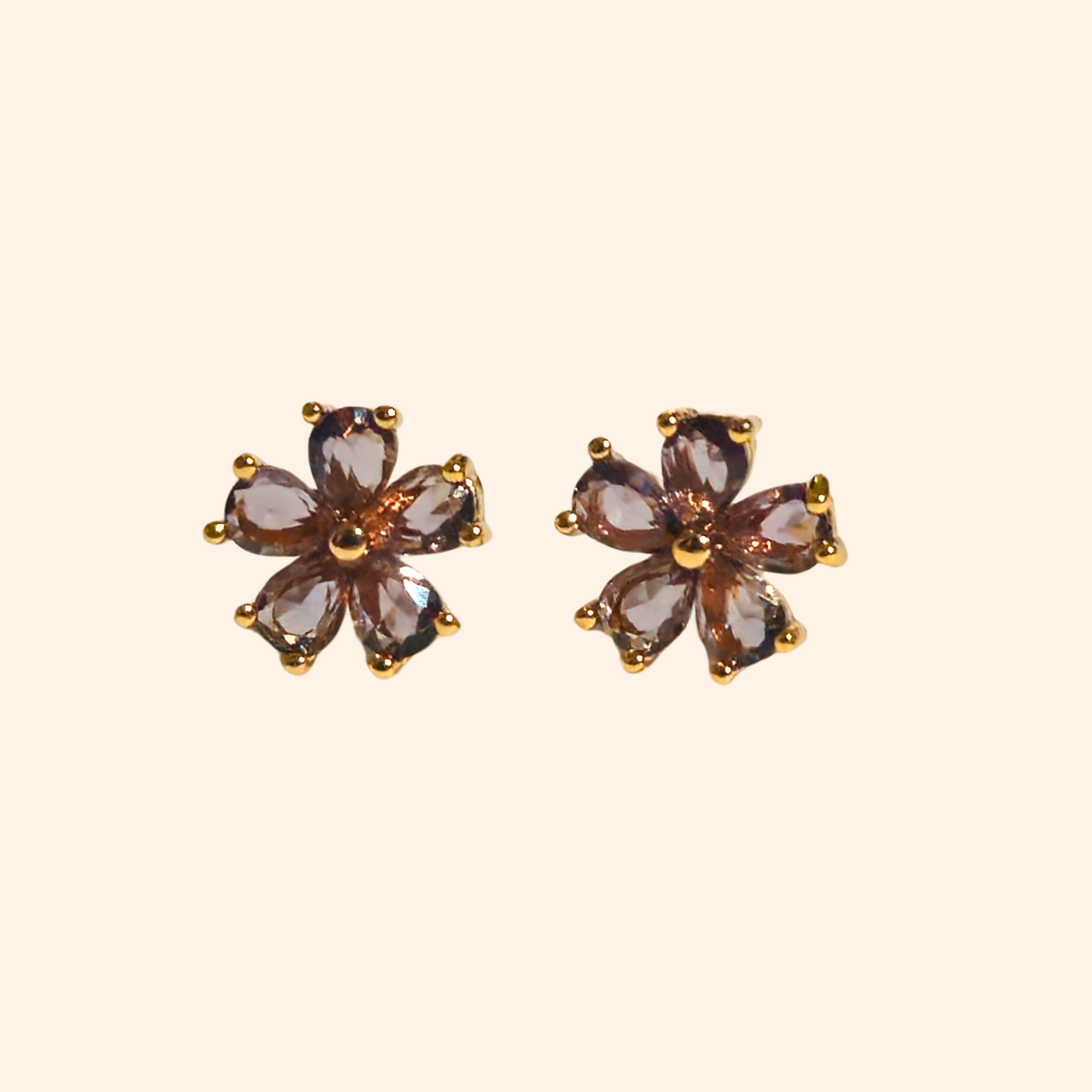 The Flowers Earrings by Roots Jewellery, featuring flower-shaped designs with purple petals and gold settings, provide a distinctive style when viewed from the front and side. These earrings are a chic complement to any ensemble.