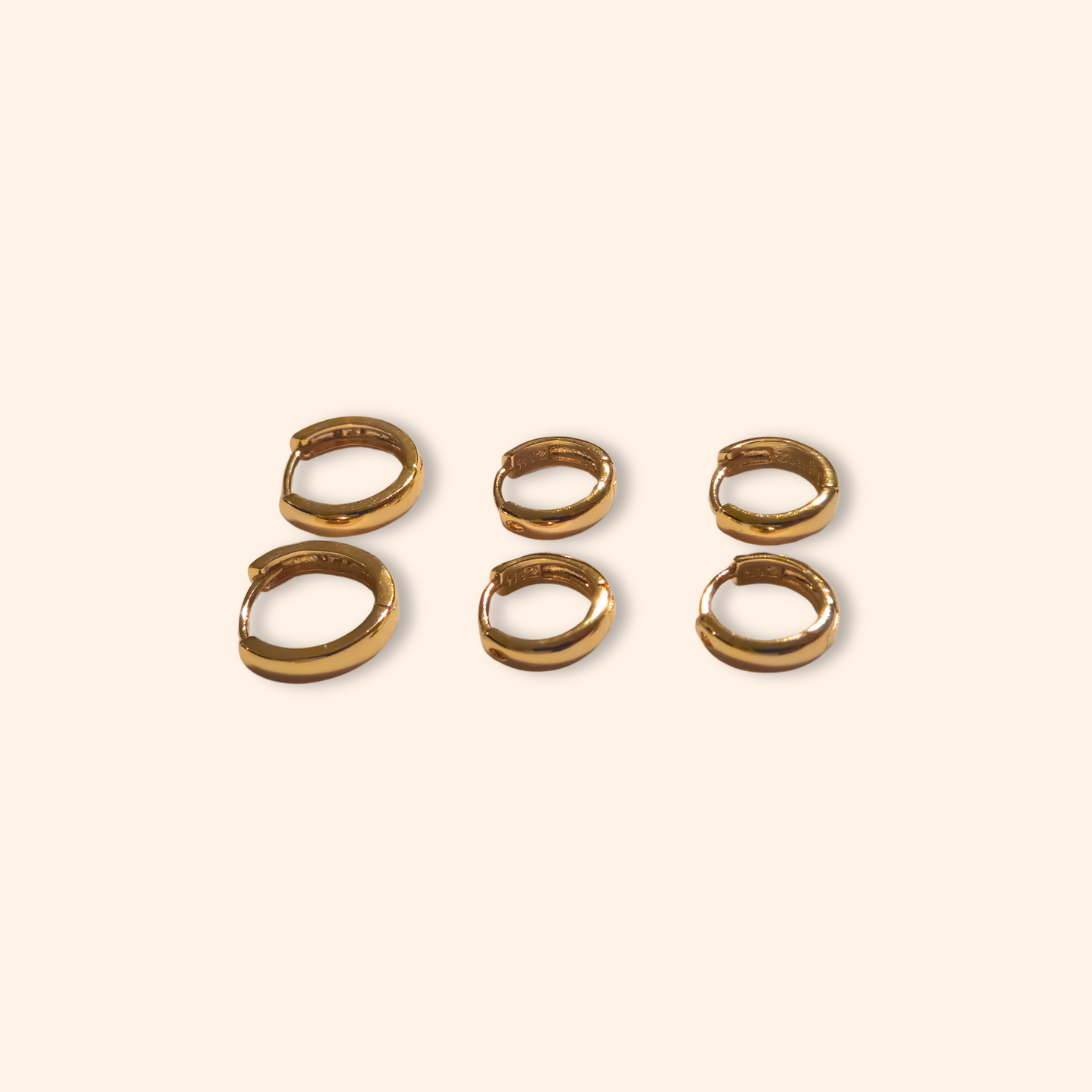 Five pairs of exquisite hoop earrings from the Roots Jewellery's "3 Set Hoop Earrings" collection gleam on a light beige background, showcasing their stunning elegance. Available in both gold and silver finishes, these elegant pieces are perfect for any occasion.