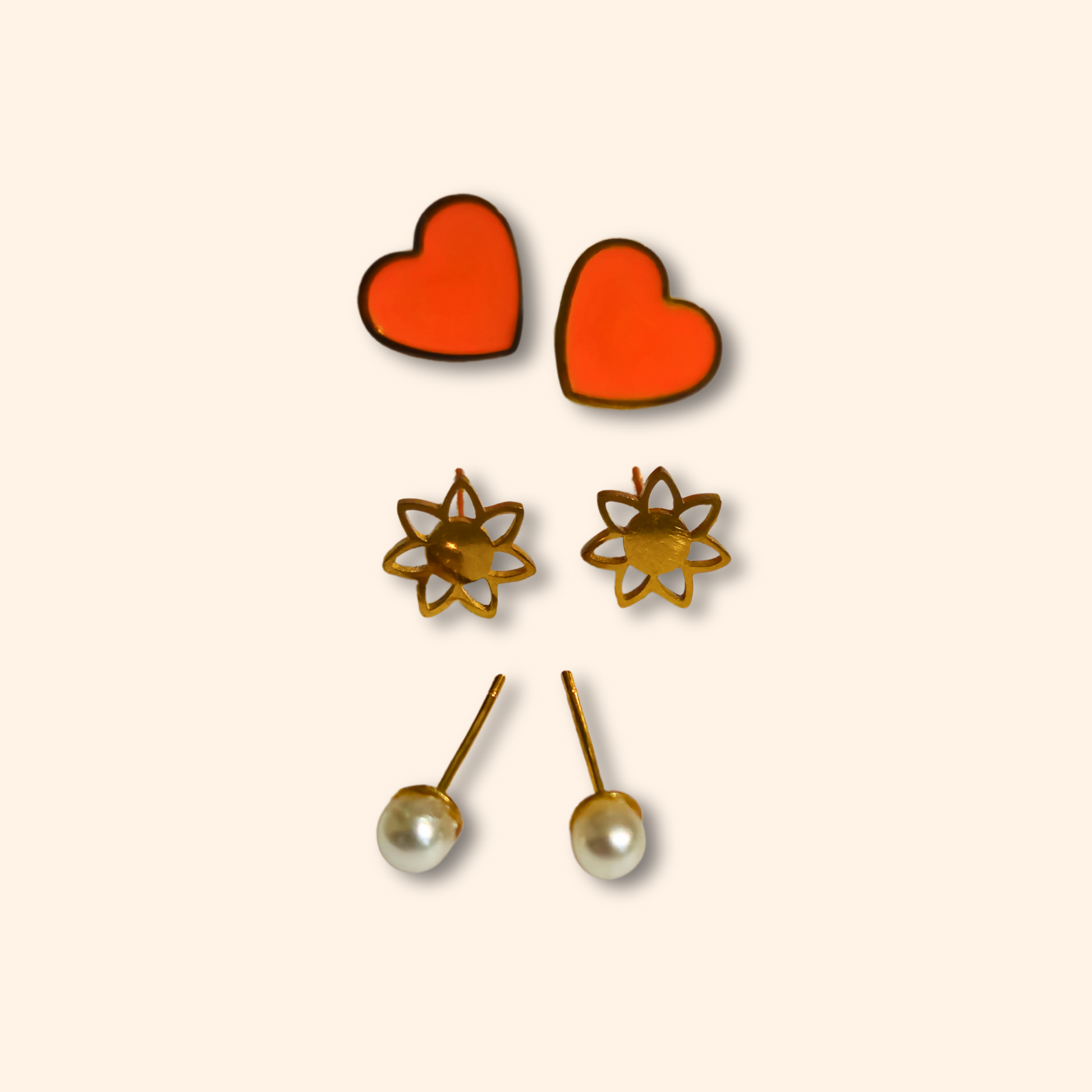 Introducing the Earring Set - Orange Hearts by Roots Jewellery: three exquisite pairs of earrings, including orange heart-shaped, gold flower-shaped, and white pearl studs, all beautifully displayed on a simple backdrop.