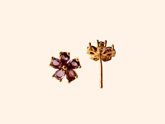 The Flowers Earrings by Roots Jewellery, featuring flower-shaped designs with purple petals and gold settings, provide a distinctive style when viewed from the front and side. These earrings are a chic complement to any ensemble.